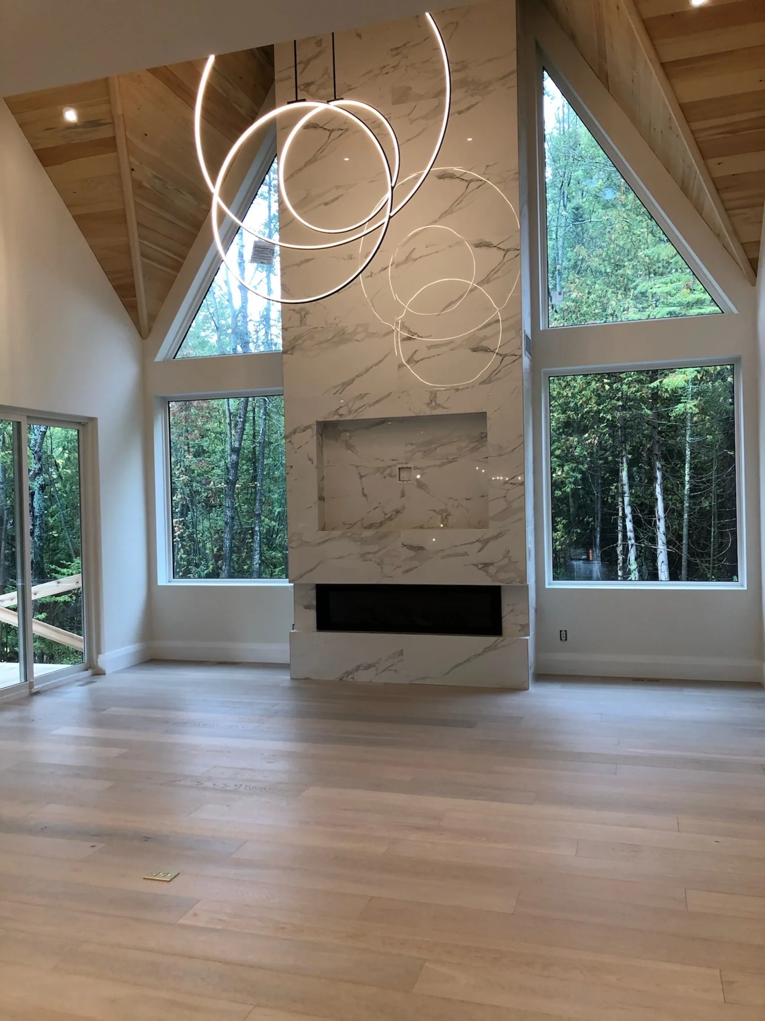 Light hardwood flooring in a vaulted great room with large windows and a marble fireplace.