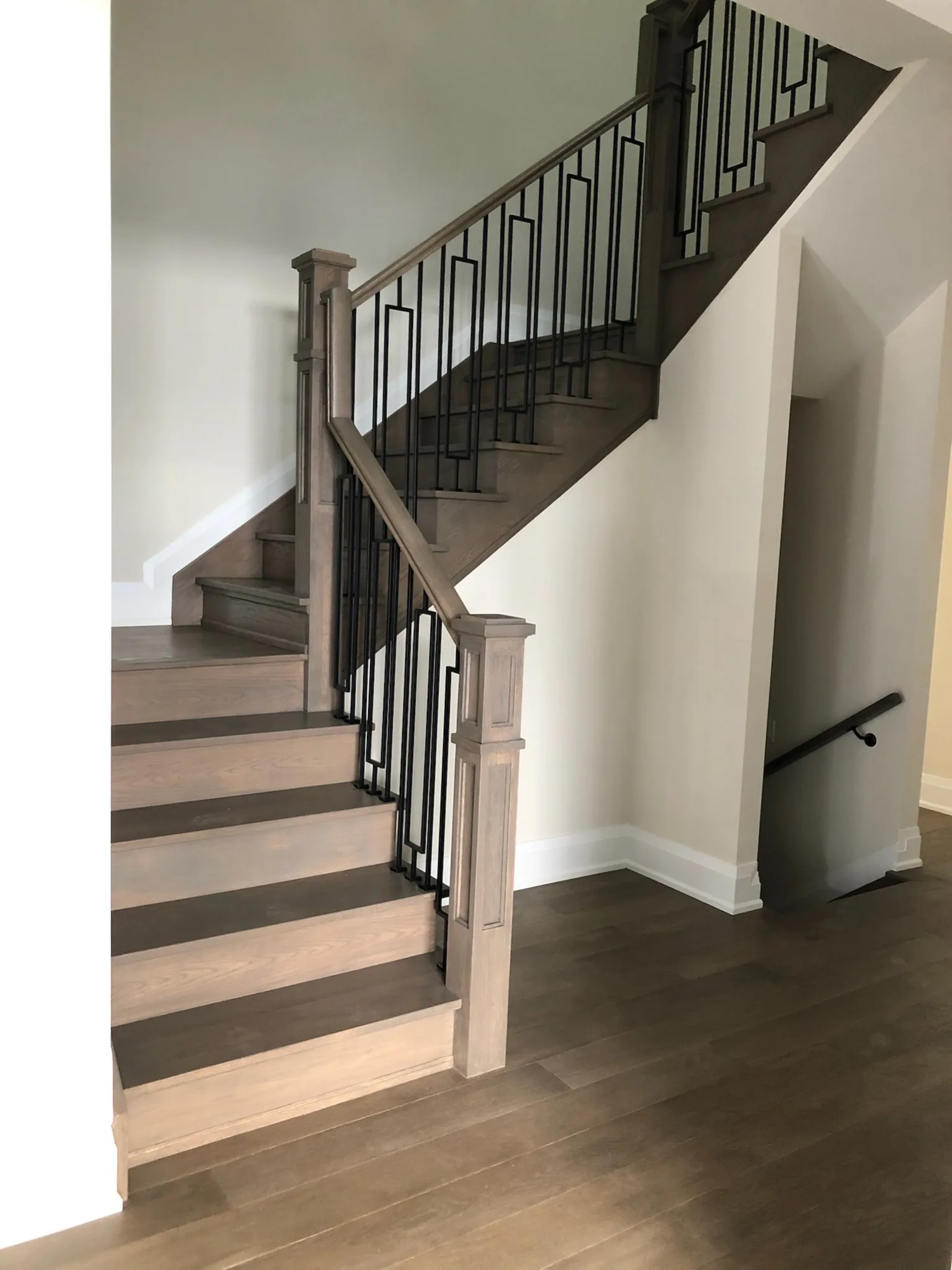 Custom stained wood staircase with geometric black metal railing and matching hardwood floor.