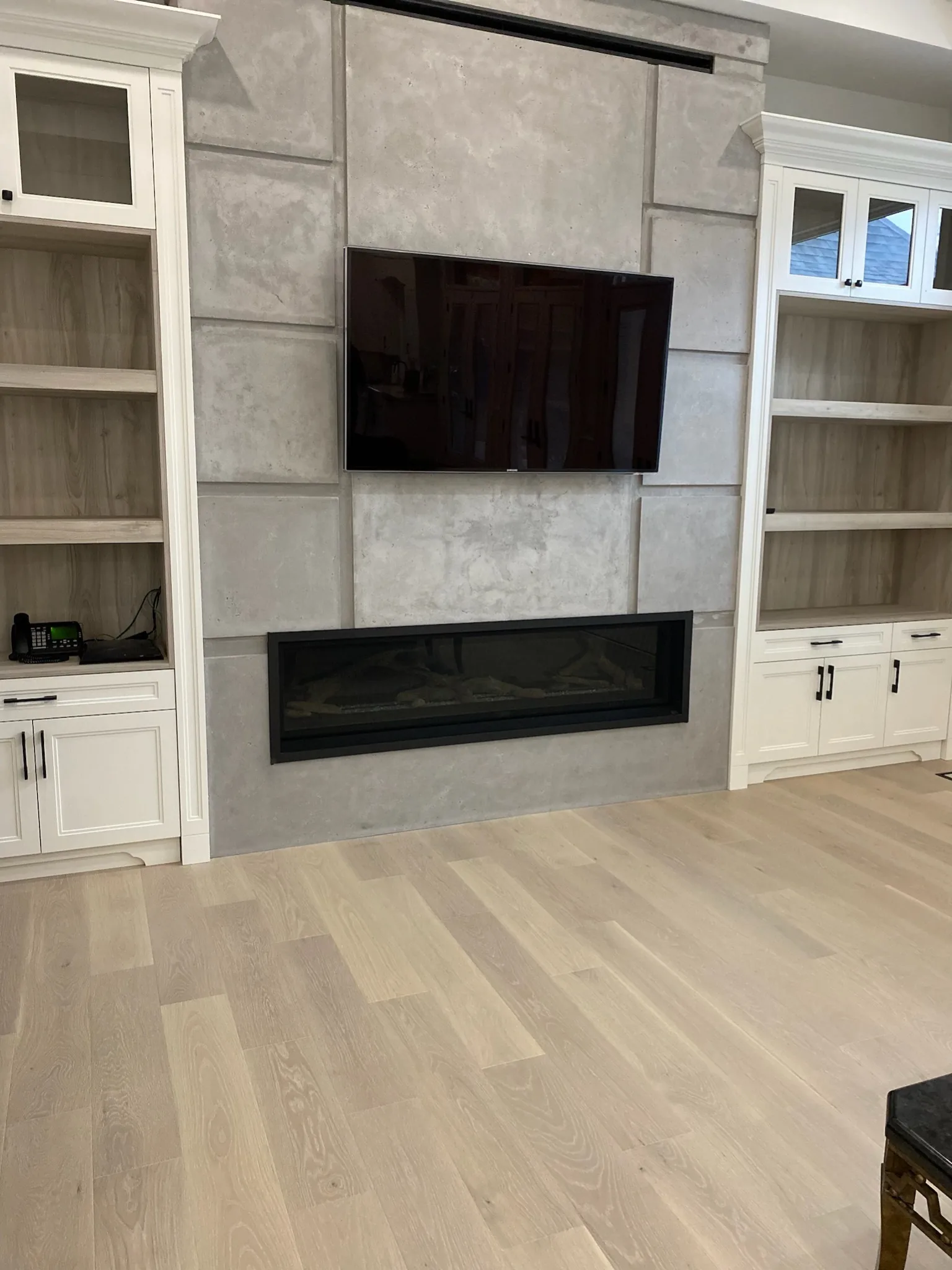 Light oak flooring in a living room with a modern fireplace and white built-in cabinetry.