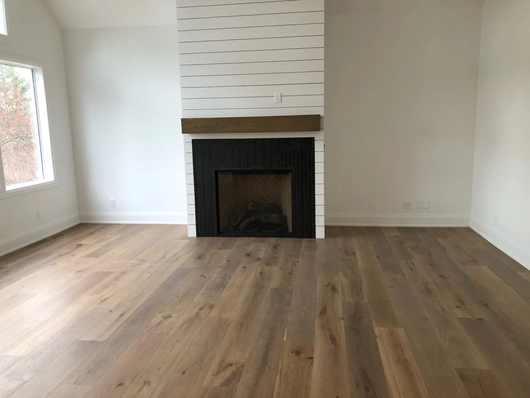 Wide-plank hardwood flooring in a bright room with a white fireplace.