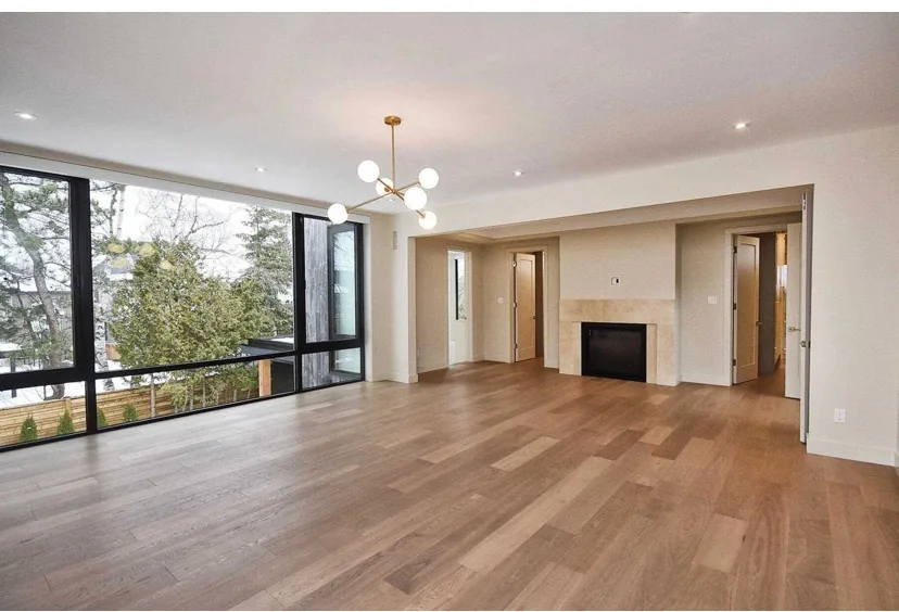 Wood plank flooring in an unfurnished room with large windows and a fireplace.