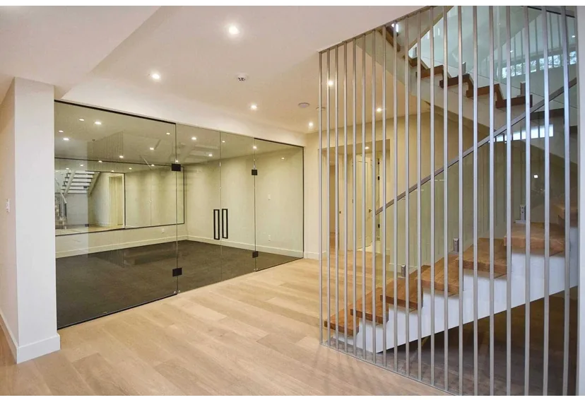 Wood flooring on a landing beside vertical stair rails and a glass-walled room.