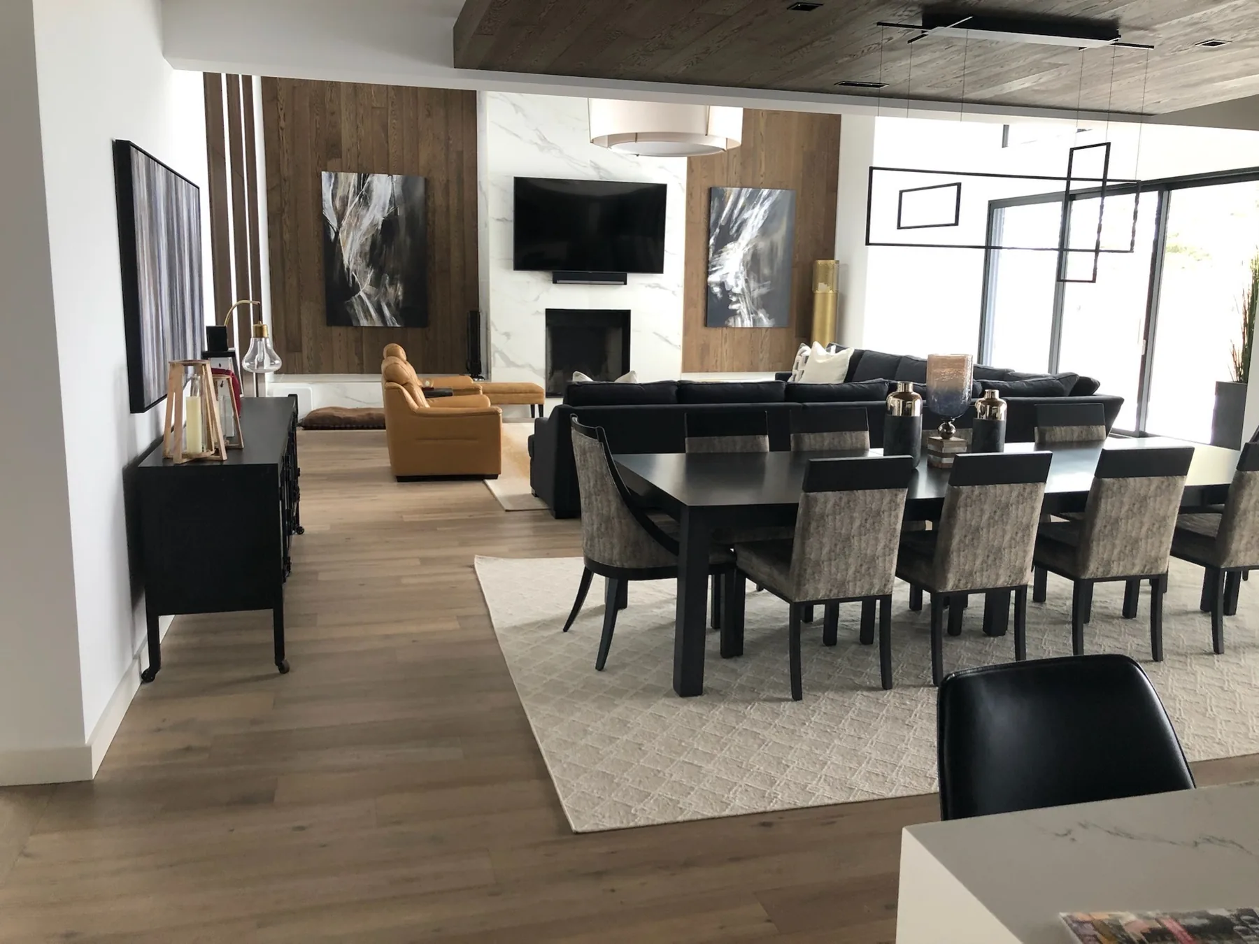 Open-plan dining and living room with wide-plank flooring and dark modern accents.