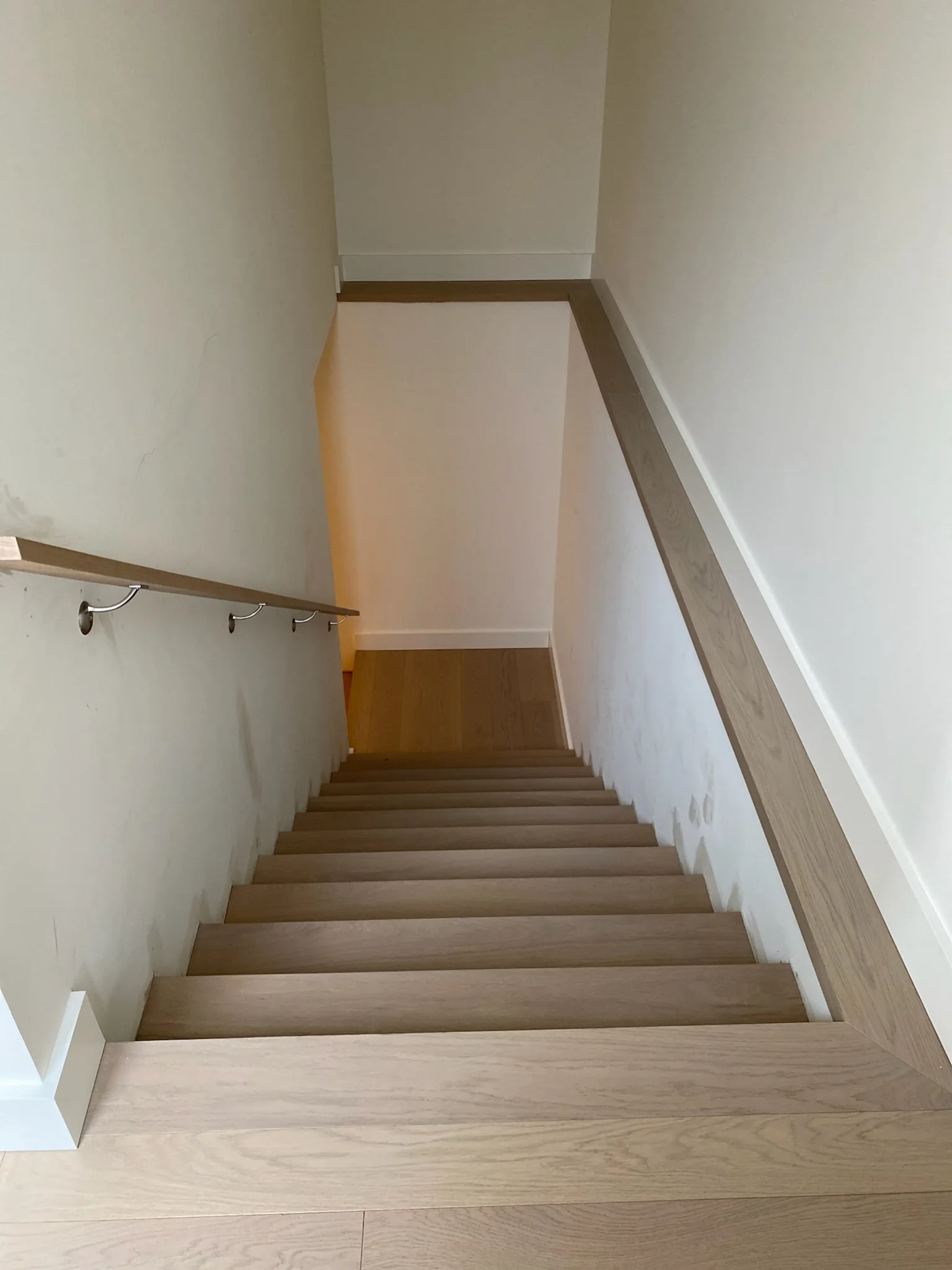 Light oak staircase descending between white walls with matching wood handrail.