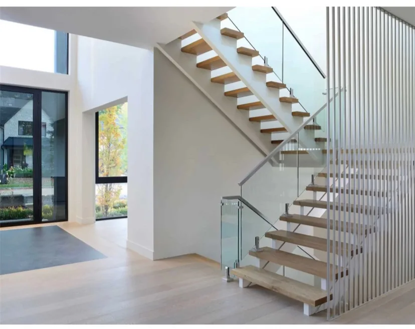 Wood stair treads and adjoining flooring beside a glass railing and vertical metal rails.