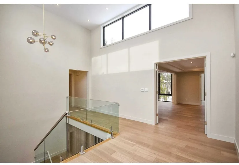 Wood flooring across an upper landing beside a glass stair railing.